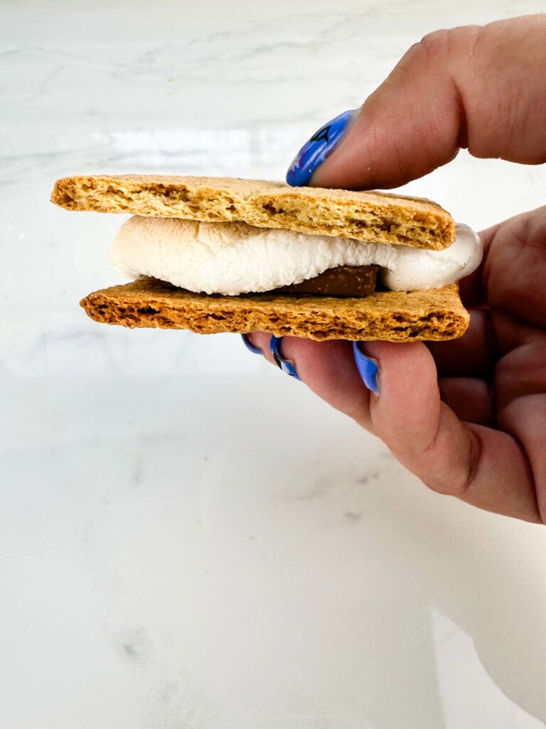 Smooshed smore between fingers with more smores in the background.