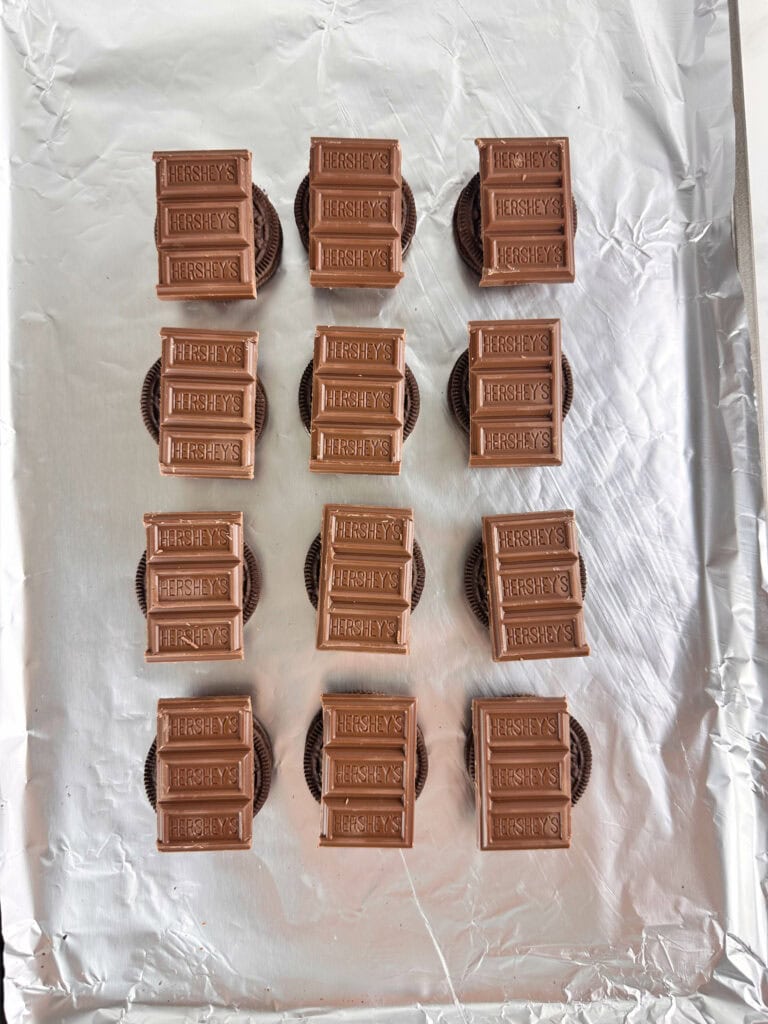 Hershey's chocolate on top of Oreos on a lined cookie sheet.