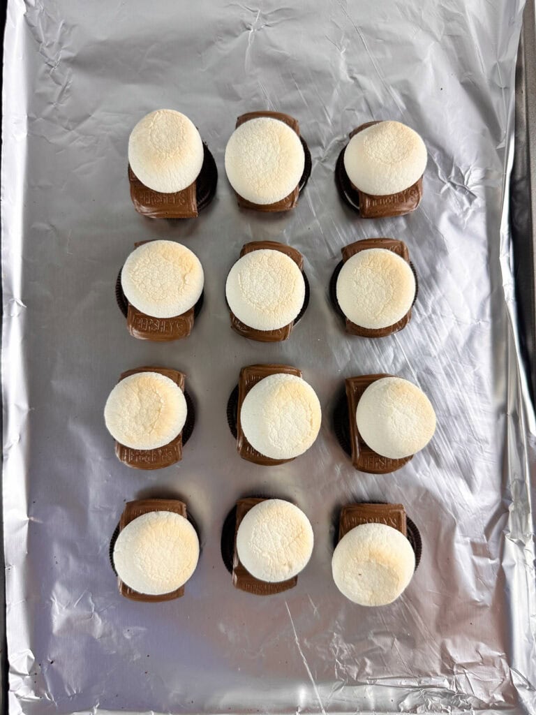 Baked marshmallows and melted chocolate on top of Oreo cookies on a cookie sheet.