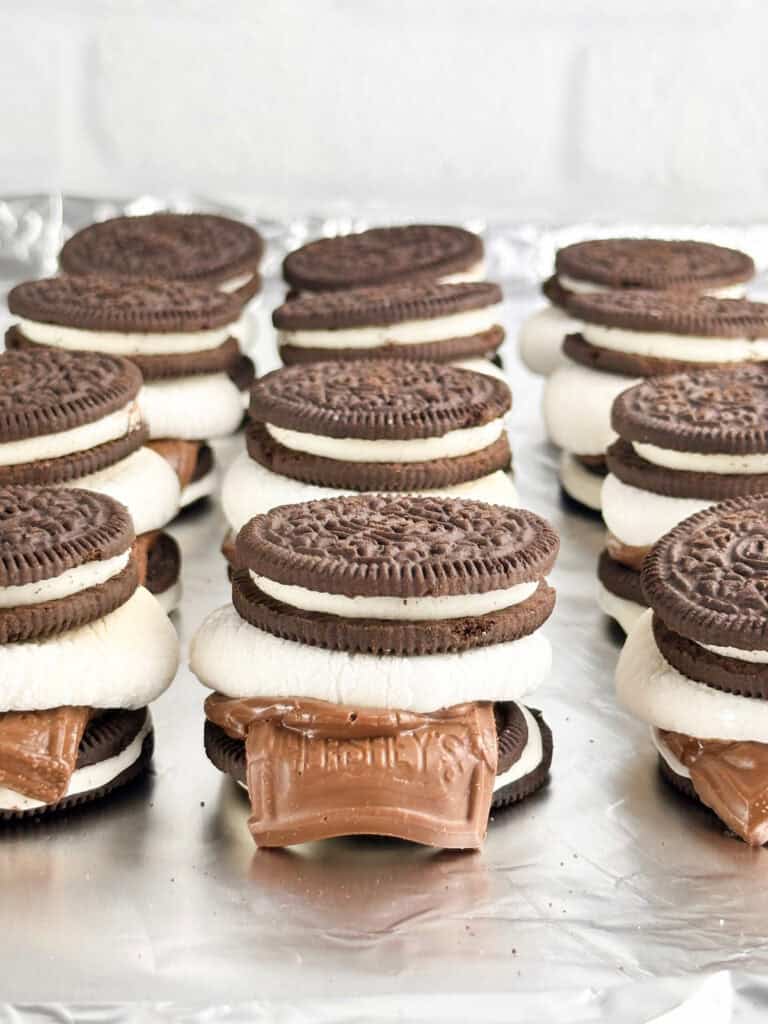 Oreo smores in a row on a cookie sheet in front of a neutral background.