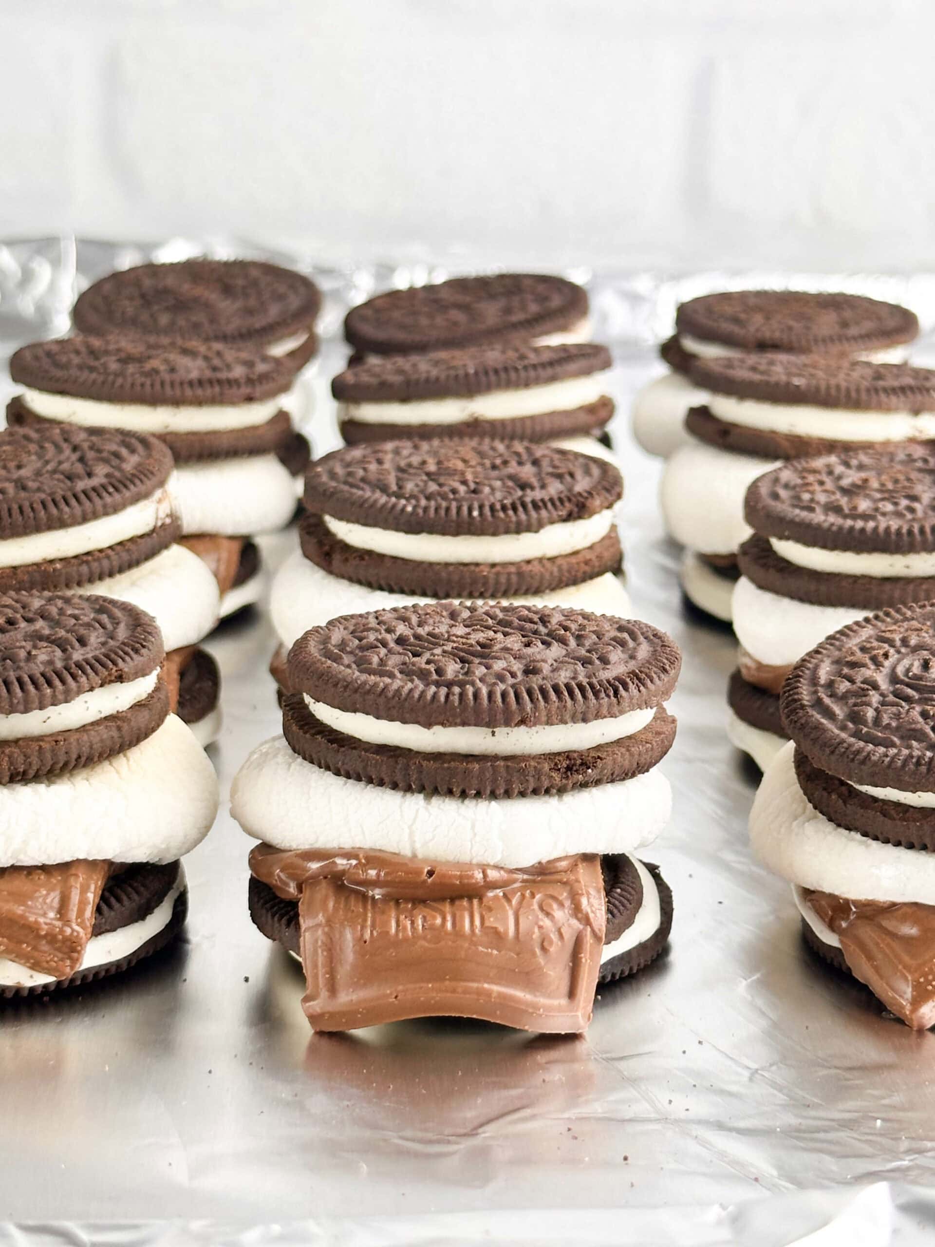 Oreo smores in a row on a cookie sheet in front of a neutral background.