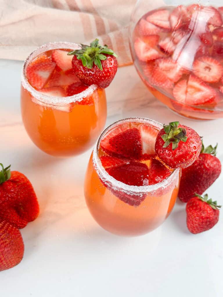 Two glasses and a pitcher of strawberry sangria, strawberries are in both glasses and pitcher.