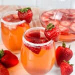 Two glasses and a pitcher of strawberry sangria, strawberries are in both glasses and pitcher.