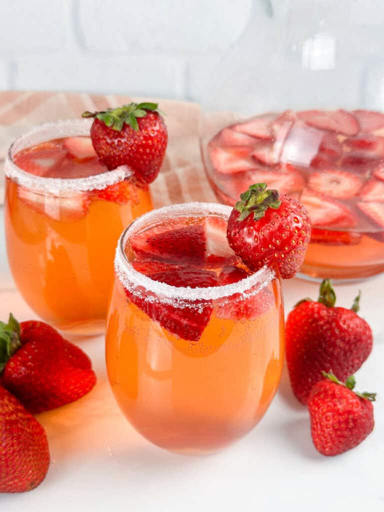 Two glasses and a pitcher of strawberry sangria, strawberries are in both glasses and pitcher.