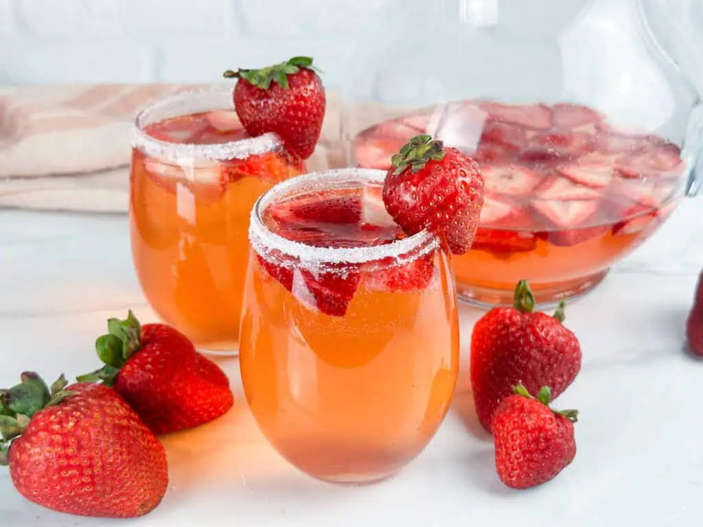 Two glasses and a pitcher of strawberry sangria, strawberries are in both glasses and pitcher.