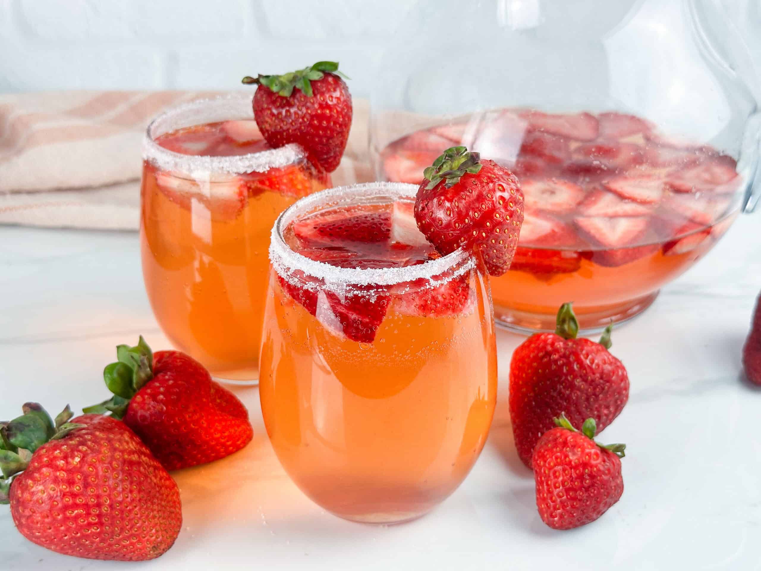 Two glasses and a pitcher of strawberry sangria, strawberries are in both glasses and pitcher.