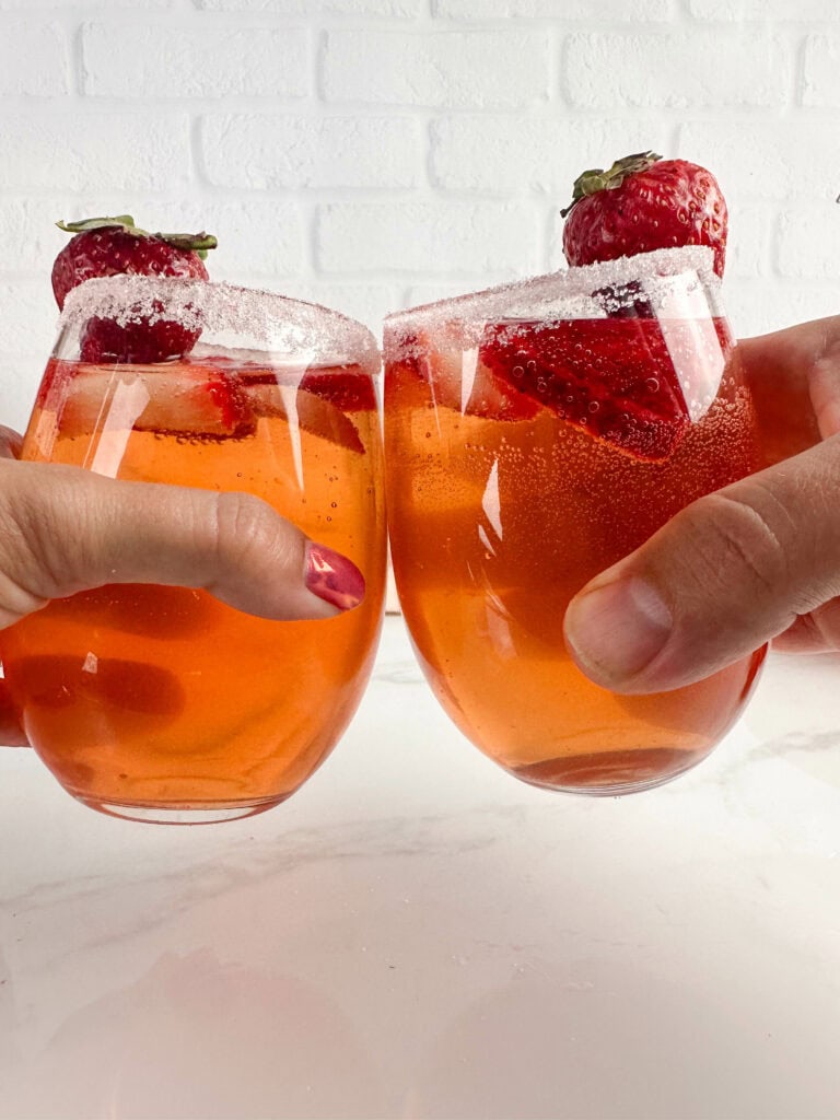 Clinking two glasses of strawberry sangria.