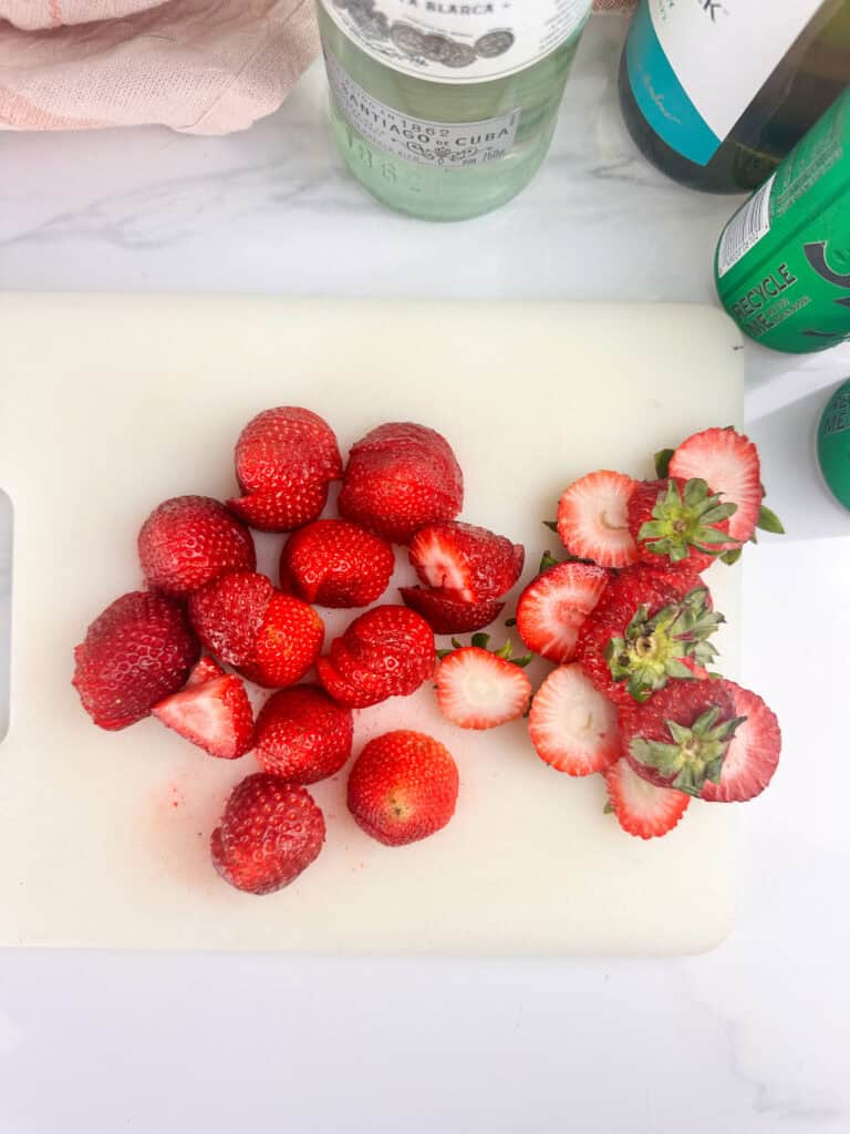 Strawberries sliced on white cutting board.