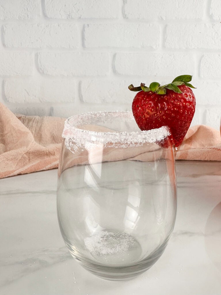 Clear wine glass with a frosted top and strawberry in front of neutral background.