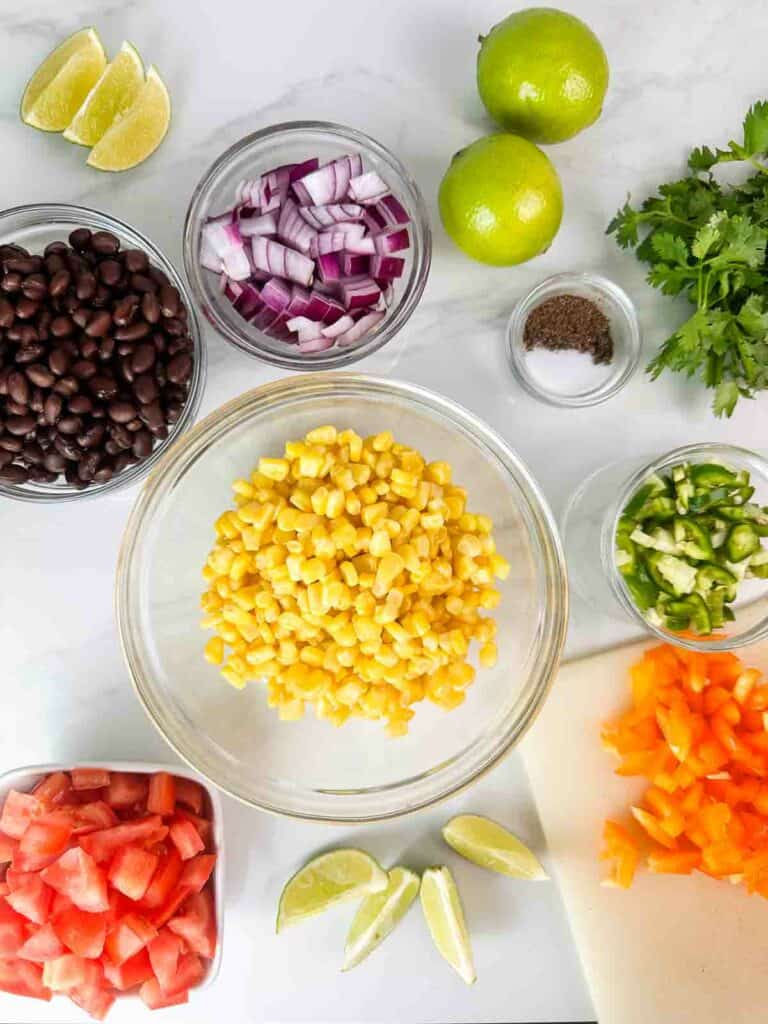 Ingredients for black bean and corn salsa dip: Corn, black beans, diced red onions, diced tomatoes, diced bell peppers, diced jalapenos, cilantro, limes, and salt and pepper