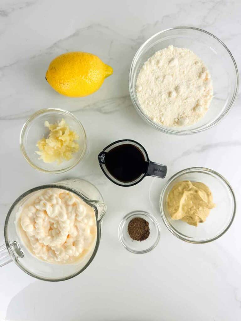 Ingredients for a homemade caesar salad dressing recipe: lemon juice, parmesan cheese, garlic, worcestershire sauce, dijon mustard, mayo, and black pepper.