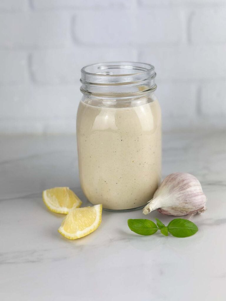 Jar of Caesar salad dressing with lemon, garlic, and basil on a neutral background in a mason jar.