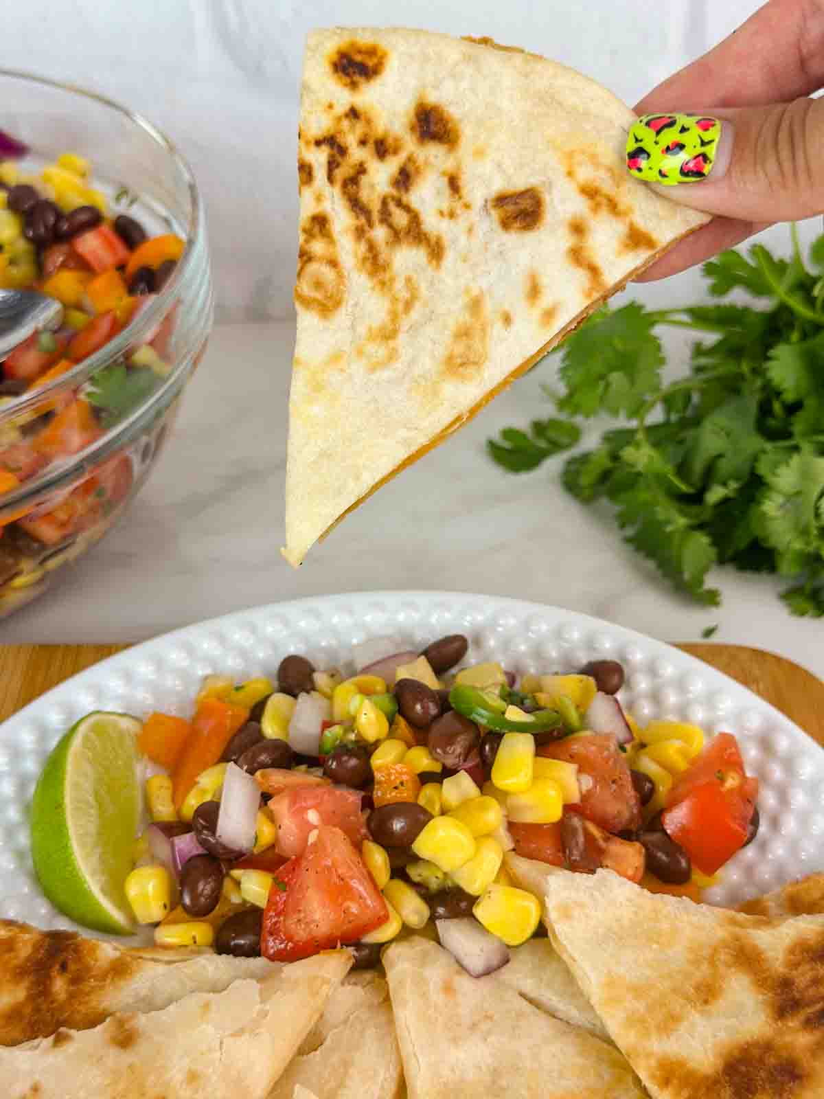 Holding a wedge of cheese quesadilla over a plate with toppings and more wedges.