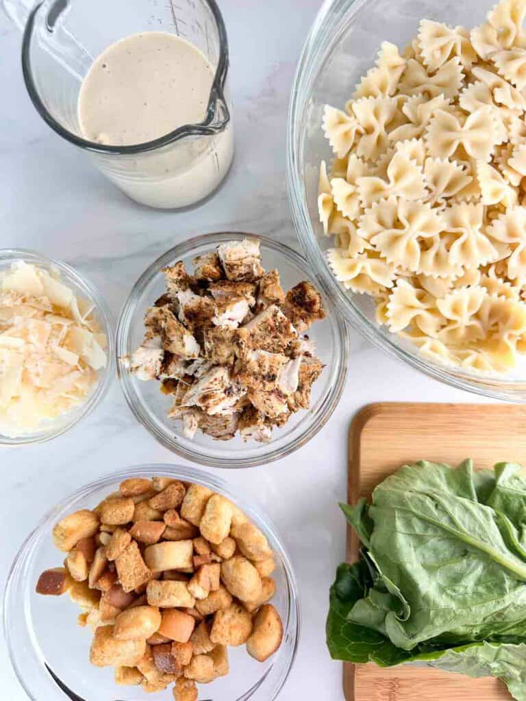 Ingredients chicken Caesar pasta salad: caesar dressing, bowtie pasta, parmesan cheese, grilled chicken, croutons, romaine lettuce.