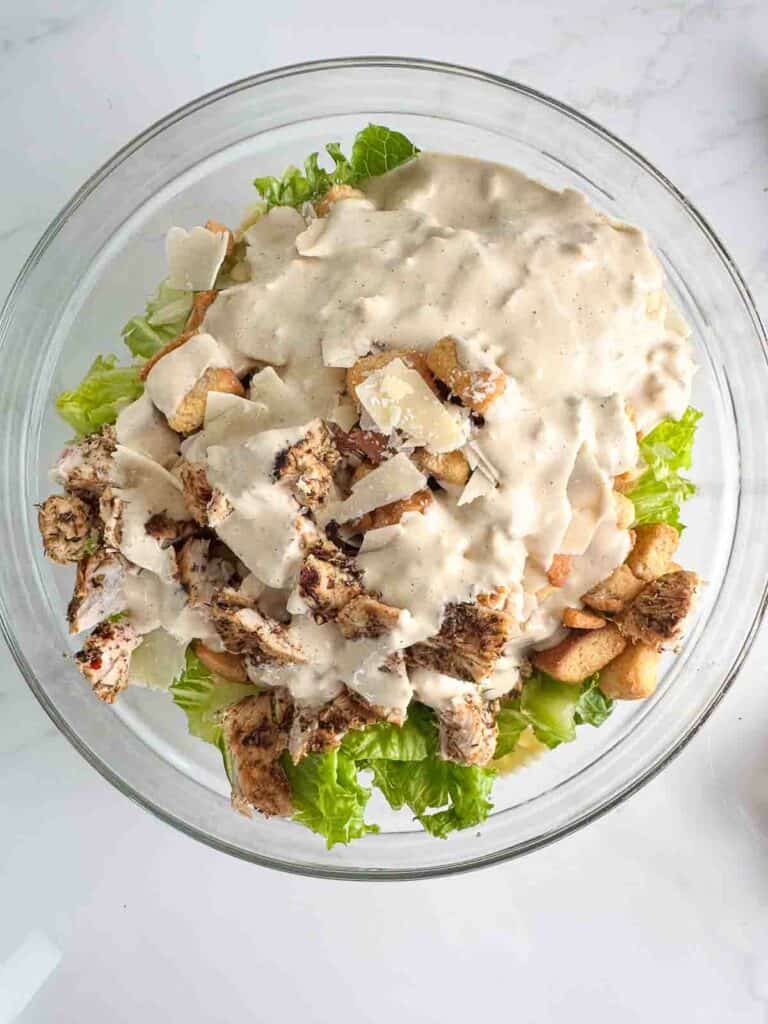 Caesar dressing on top of the ingredients for chicken Caesar pasta salad.