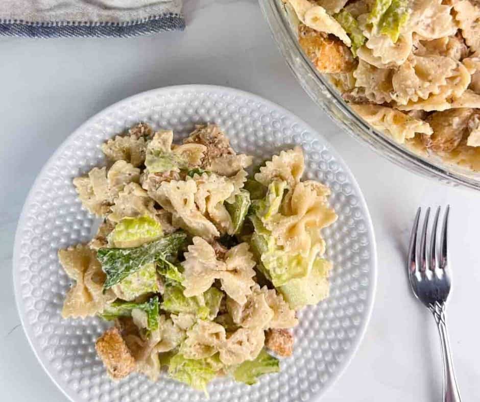 Serving chicken Caesar pasta salad on a white plate with a fork next to it.