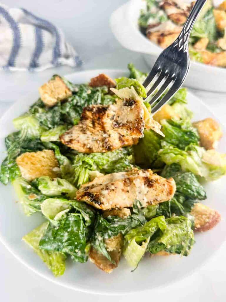 Fork of chicken Caesar salad over a plate of it.