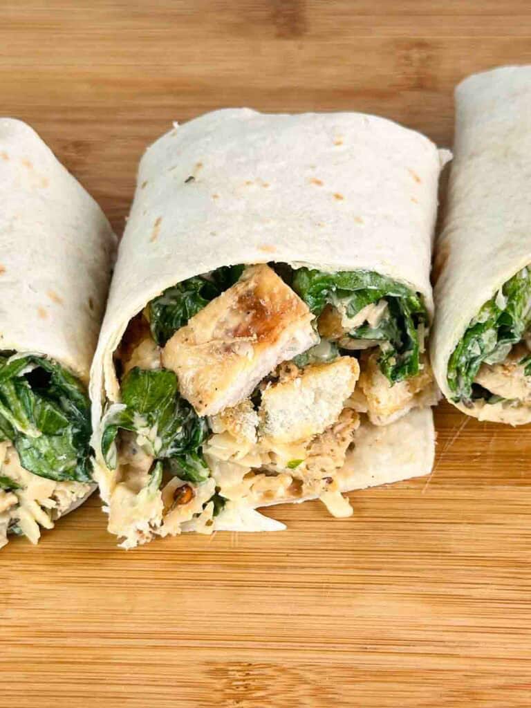 Chicken Caesar Salad Wrap cut in half on a cutting board.