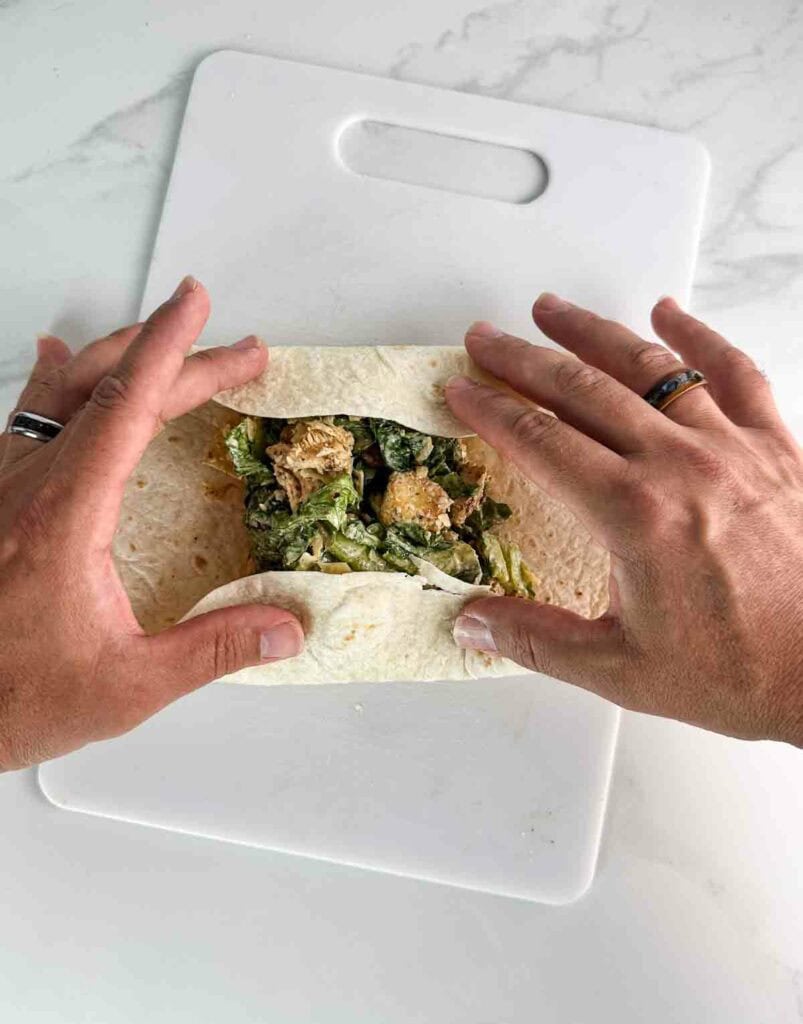 Folding in the ends of the wrap to seal the chicken caesar salad wrap when done folding.