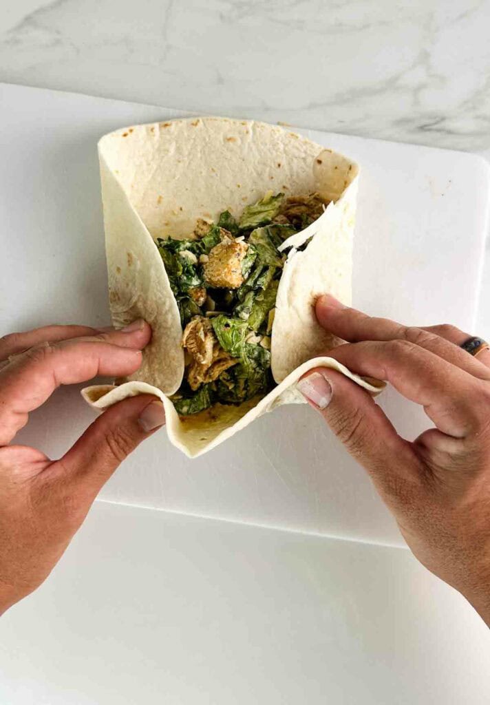 Folding a chicken caesar salad wrap .