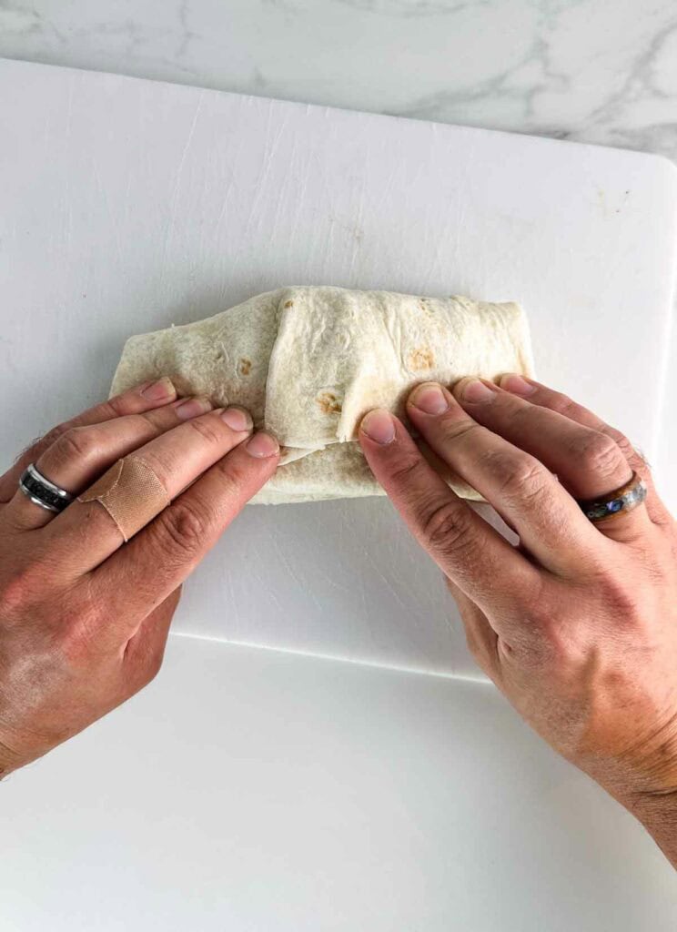 Folding a chicken casesar salad wrap on a white cutting board.