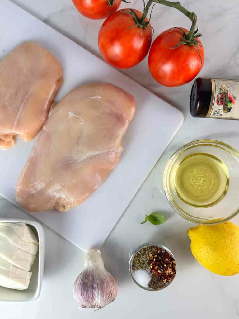Ingredients for grilled bruschetta chicken: tomatoes, chicken breasts, balsamic glaze, olive oil, mozzarella, garlic, pepper, red pepper flakes, salt, and lemon juice.