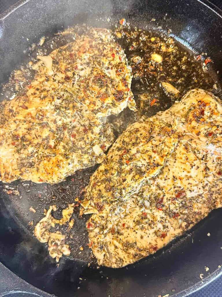 Chicken cooking in a cast iron skillet.