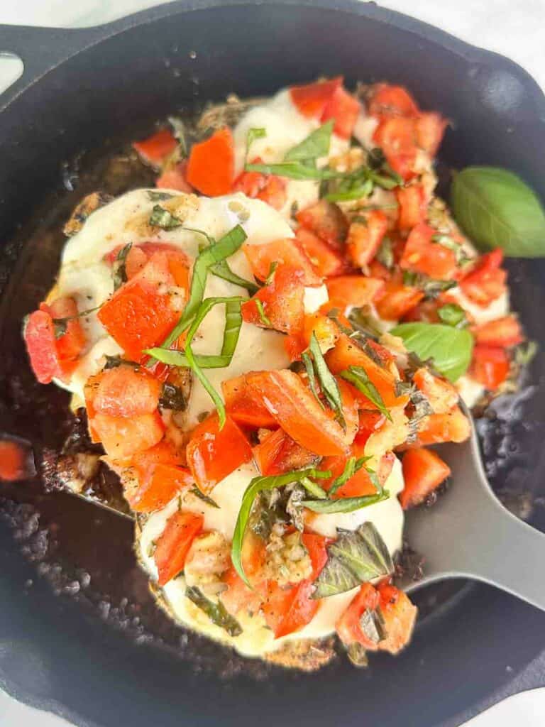 Serving of grilled bruschetta chicken held over a pan.