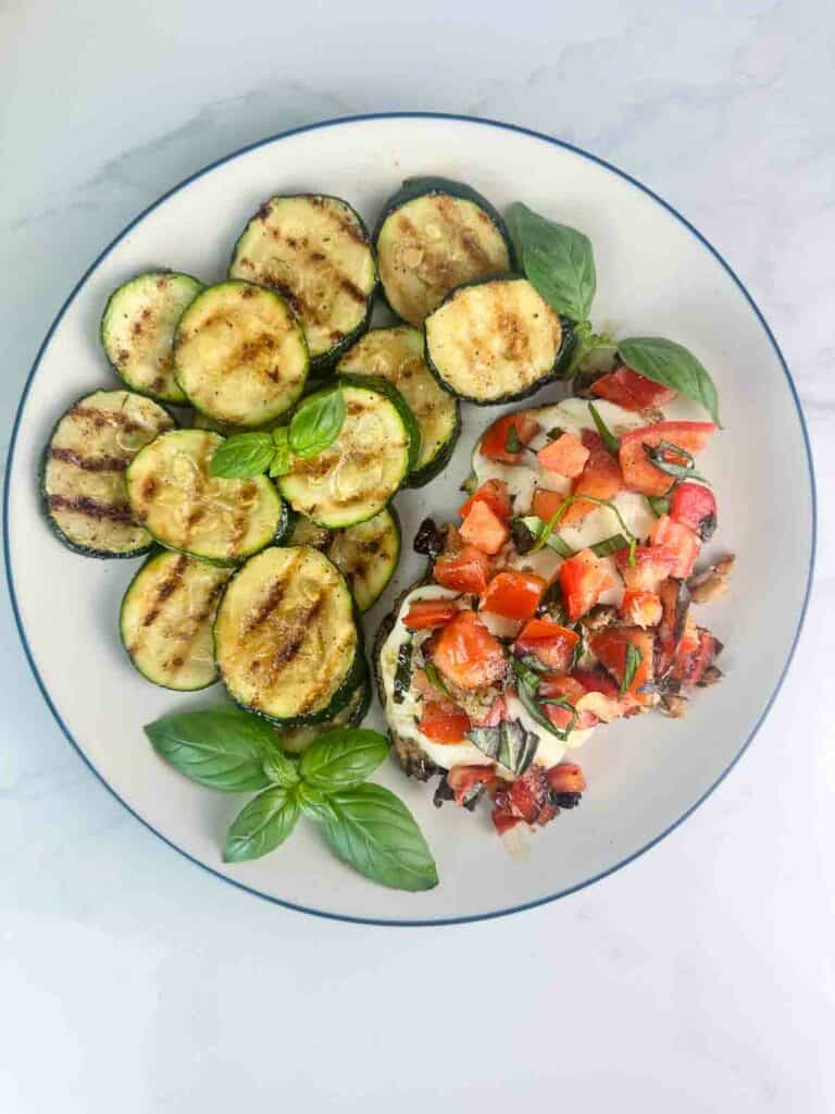 Grilled zucchini on a plate with grilled bruschetta chicken.