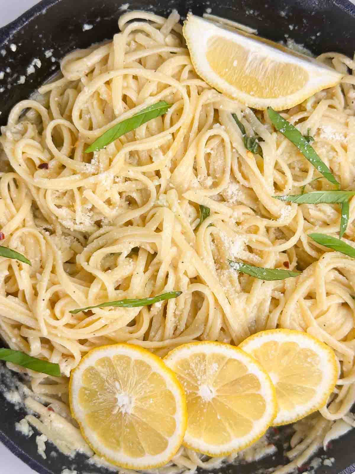 Fully tossed together lemon pasta in a cast iron skillet with basil and lemons on top.
