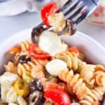 Taking a forkful of pasta salad over a white bowl of pasta salad.
