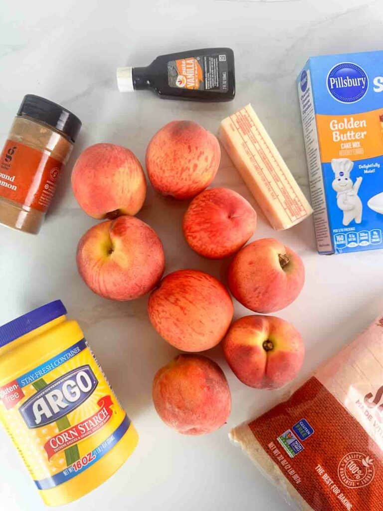 Ingredients for peach cobbler with cake mix: cinnamon, vanilla extra, cake mix, peaches, butter, corn starch, and brown sugar.