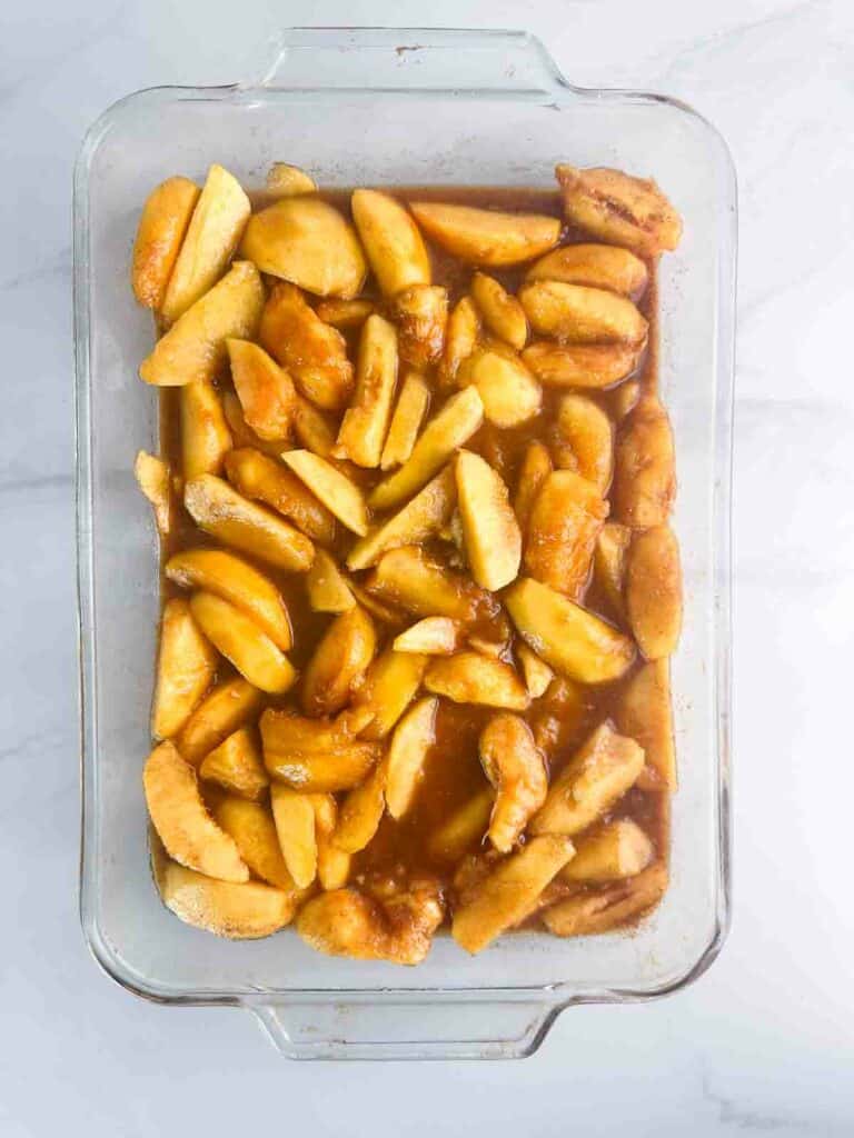 Peaches for peach cobbler spread out in a baking dish.