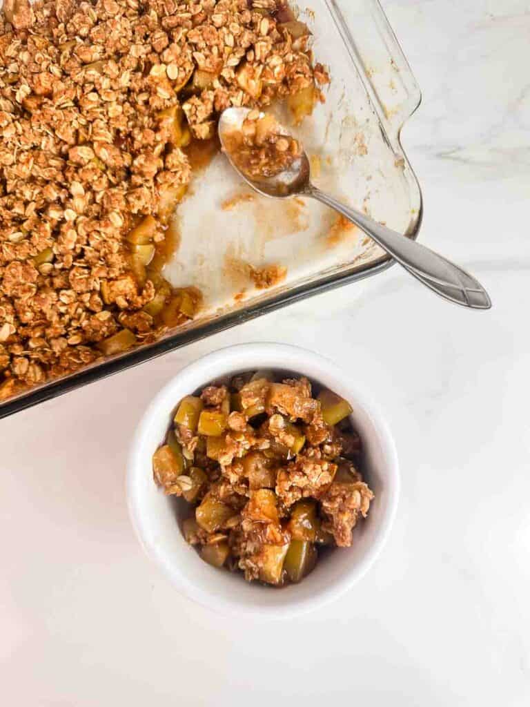 Taking a serving of apple crumble in a white bowl.