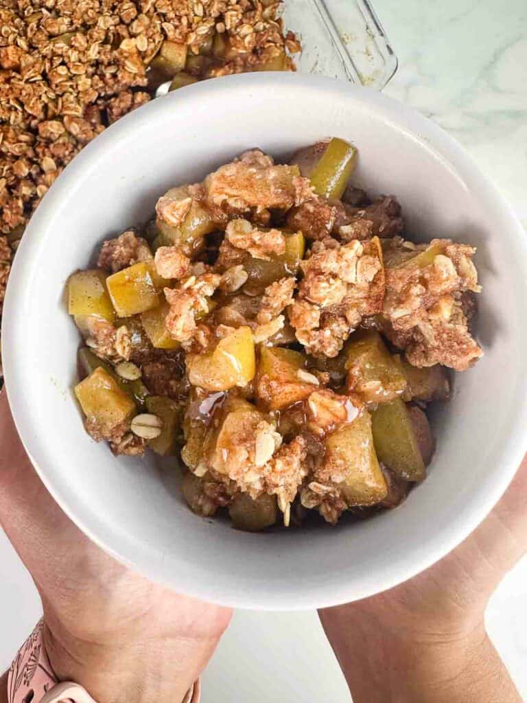 Hands holding a white bowl of apple crumble.