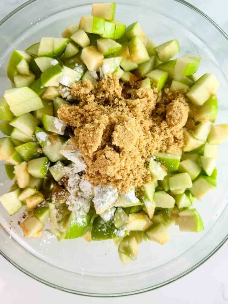 Brown sugar, corn starch, and green apples in a clear bowl.
