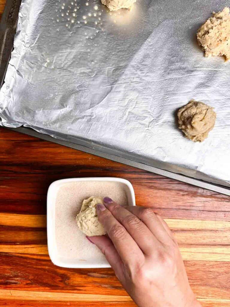 Rolling a ball of chai cookie dough in a bowl of cinnamon sugar.