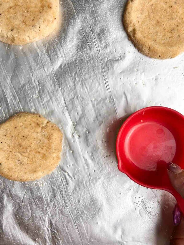 Flattening chai cookies with a red measuring cup.