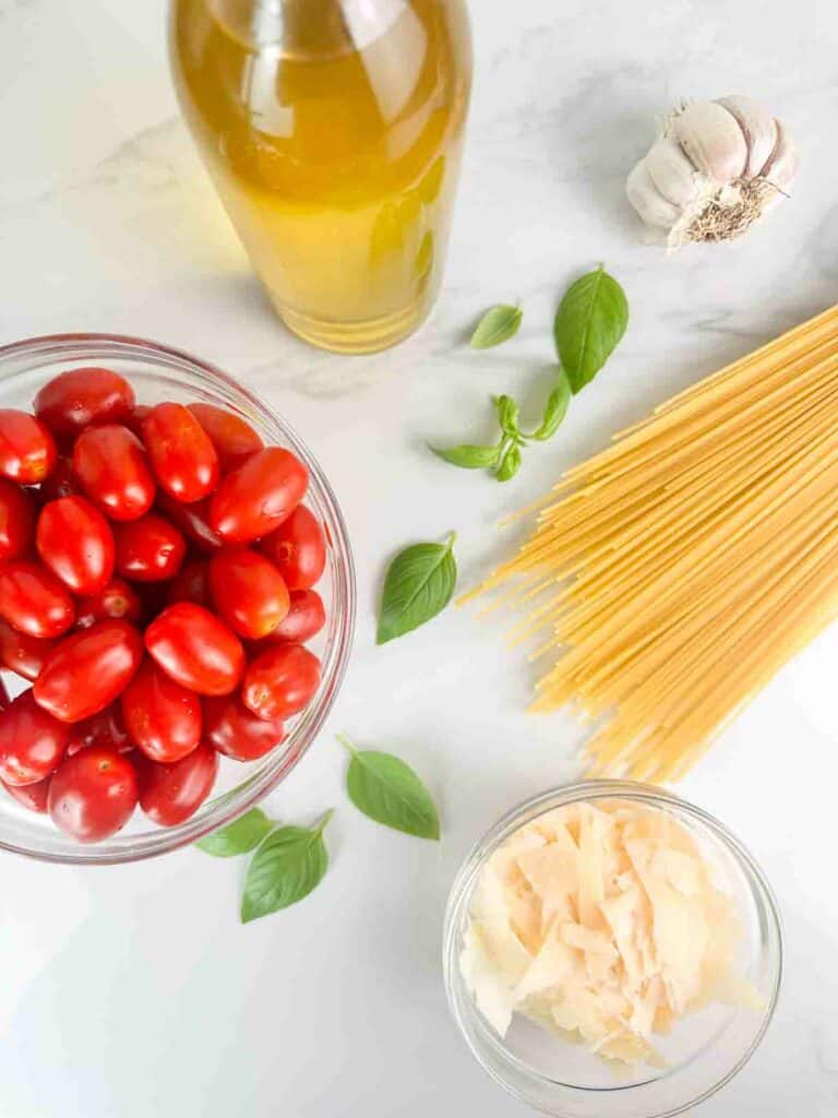 Ingredients for cherry tomato pasta: olive oil, garlic, basil, tomatoes, pasta, and parmesan cheese.