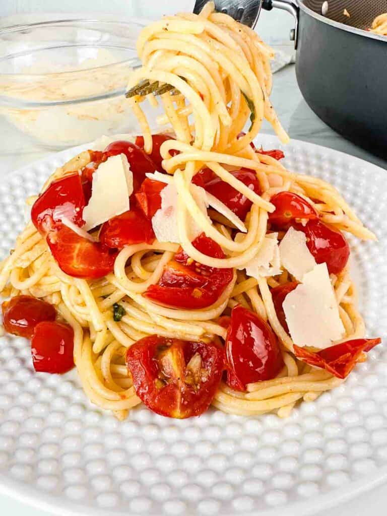 Cherry tomato pasta with basil and parmesan cheese on a white plate with a fork lifting it out