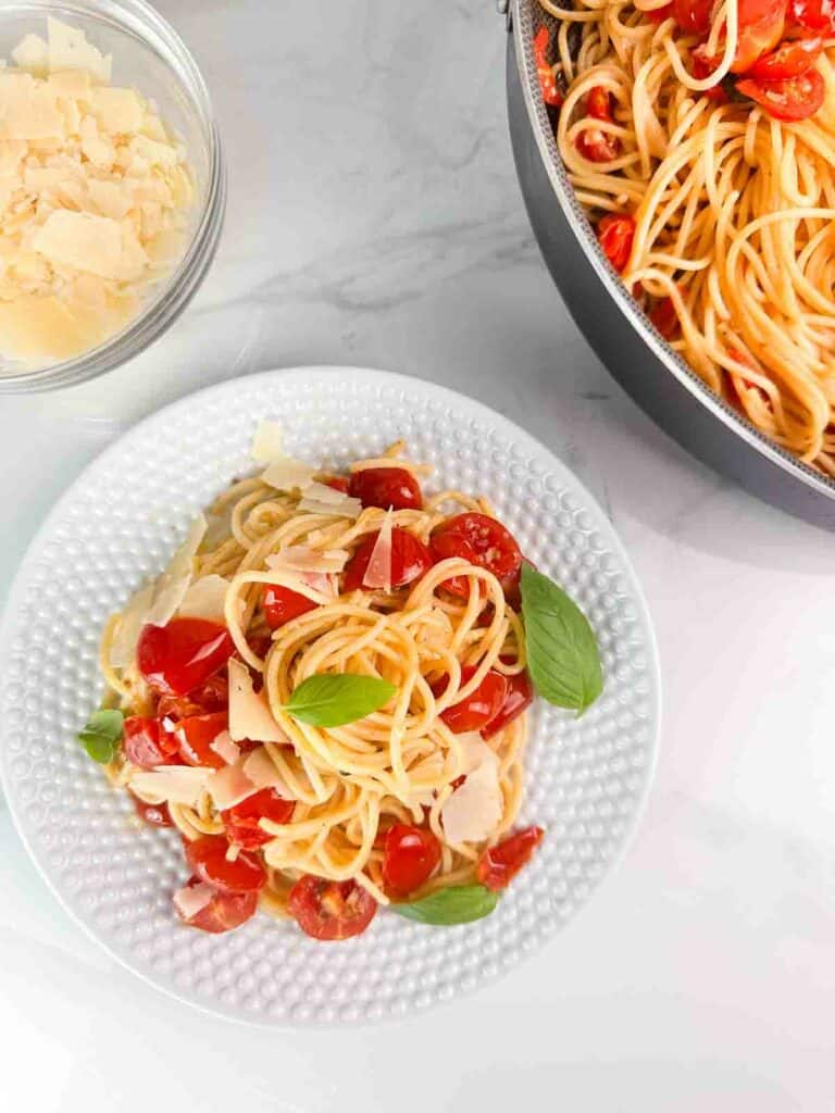 Cherry tomato pasta with basil and parmesan cheese on a white plate with the pan it was cooked in.