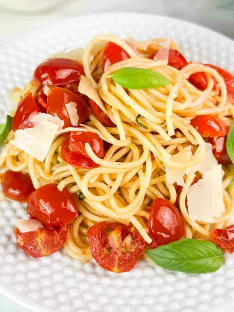 Cherry tomato pasta with basil and parmesan cheese on a white plate.