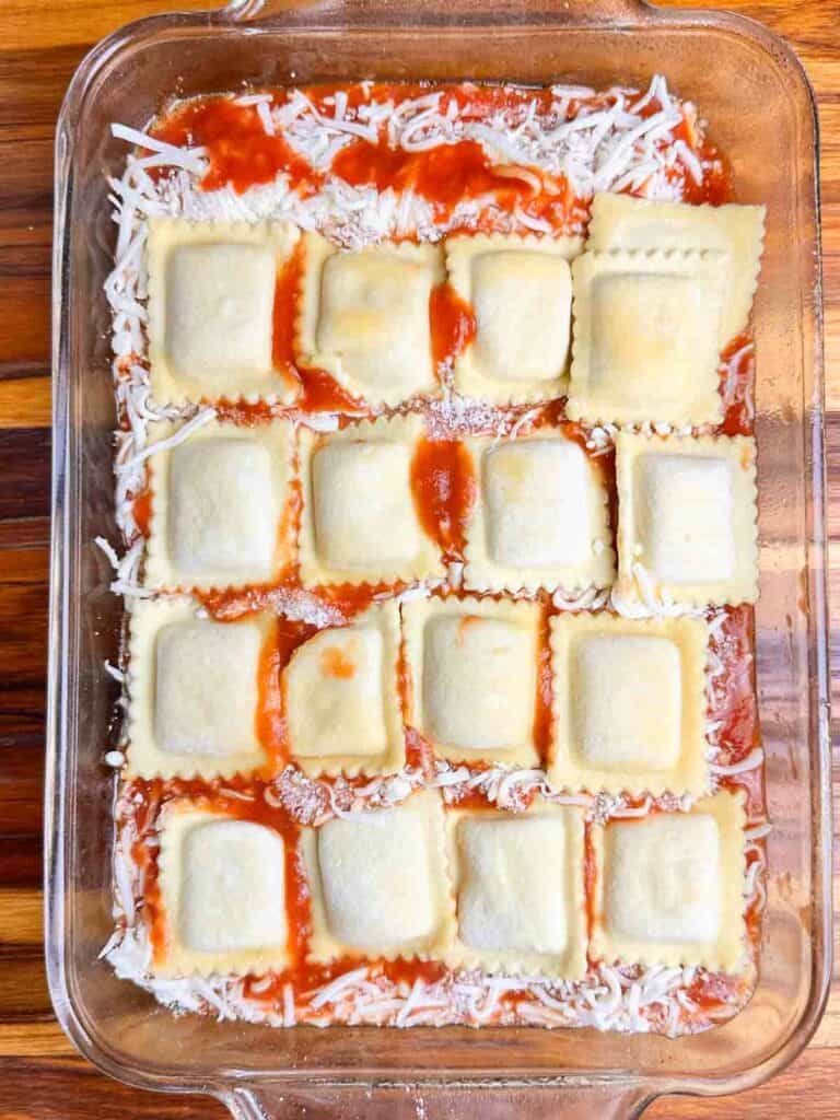 A layer of ravioli on top of sauce and cheese in a clear baking dish.