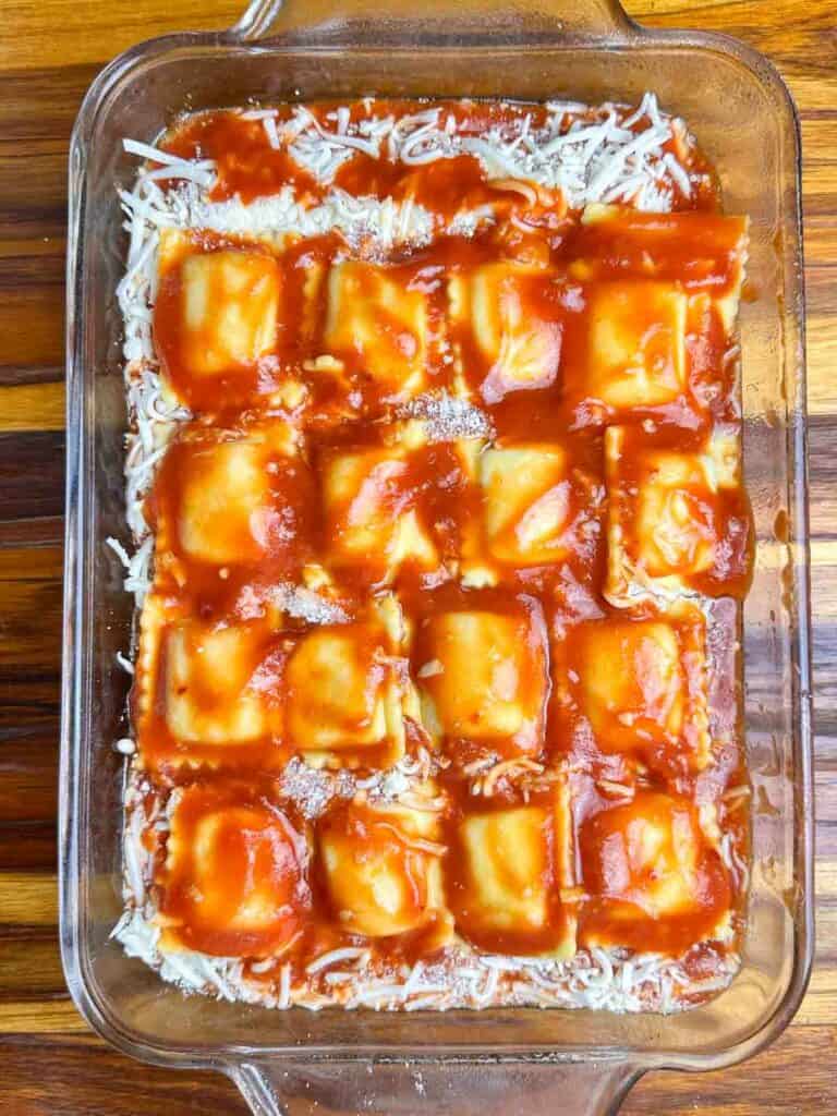 Ravioli covered with red sauce in a clear baking dish.