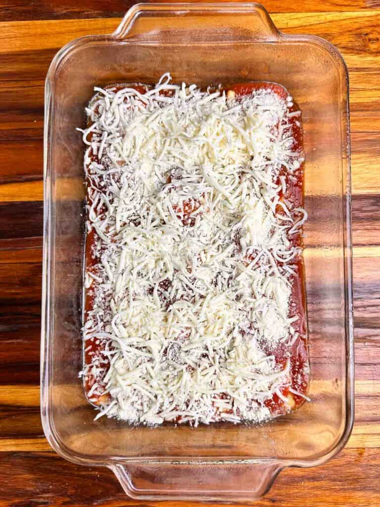 Cheese on top of red sauce in a clear baking dish.