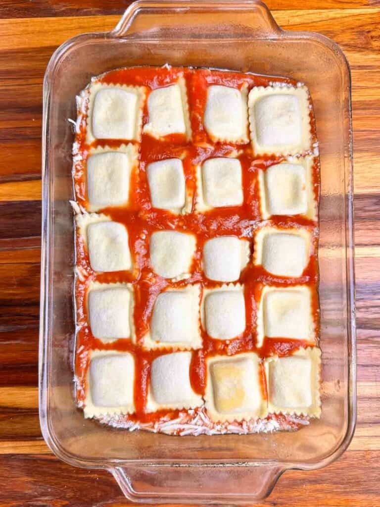 A layer of ravioli on top of sauce in a clear baking dish.