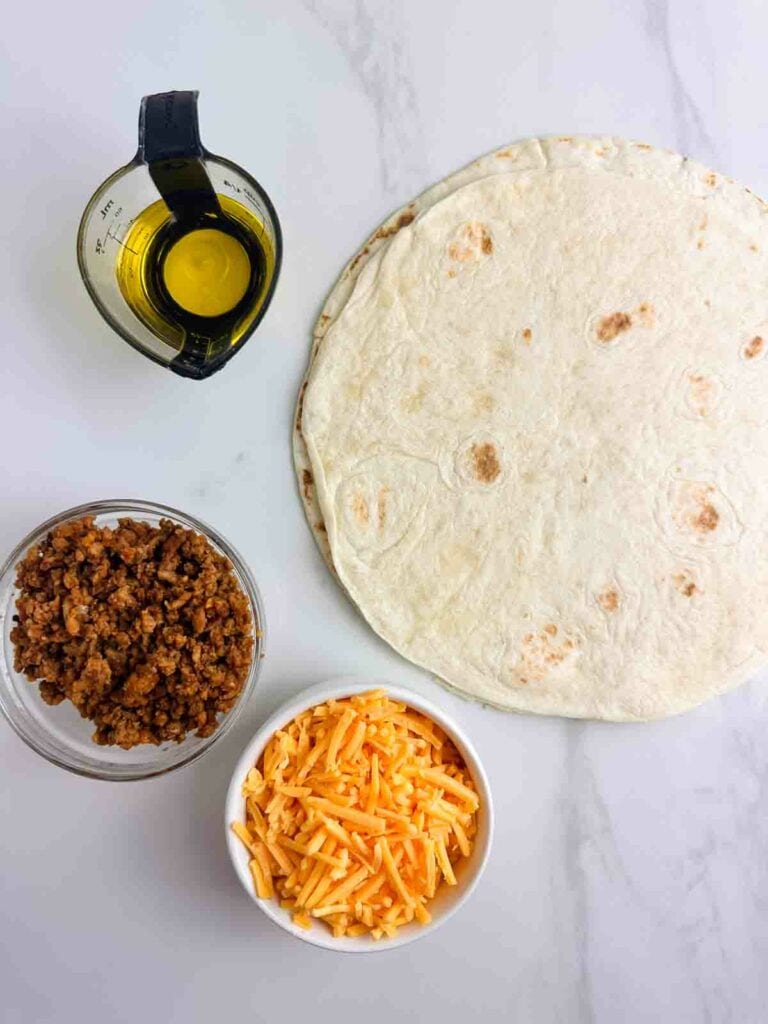 Ingredients for a chicken quesadilla recipe: olive oil, tortillas, cooked chicken, and cheese.