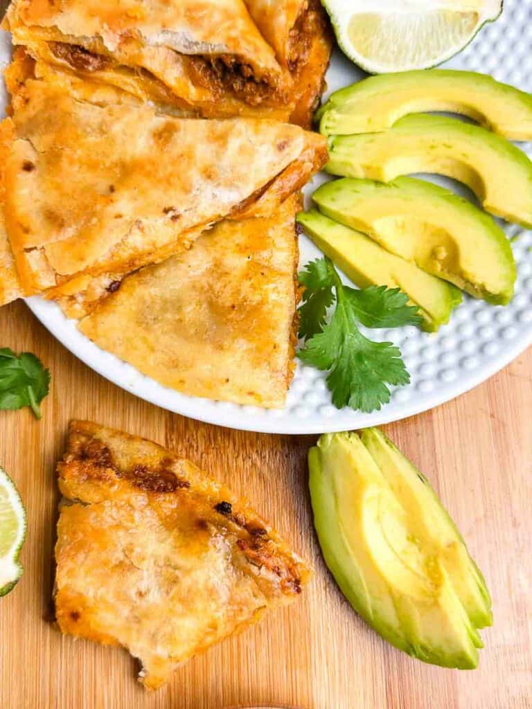 Plate of chicken quesadillas with avocado and lime.