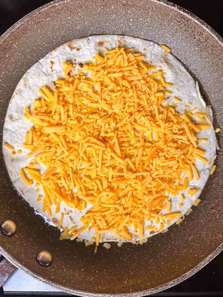 Cheese on top of a tortilla in a pan.