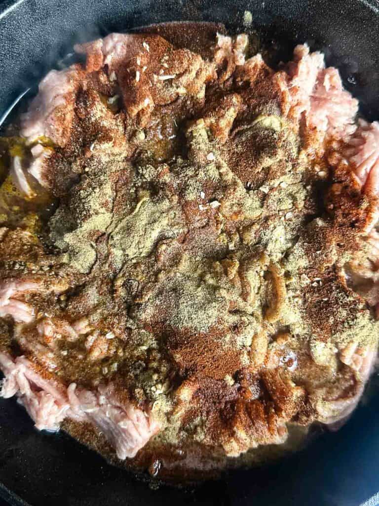 Ground chicken with seasonings in a cast iron skillet.